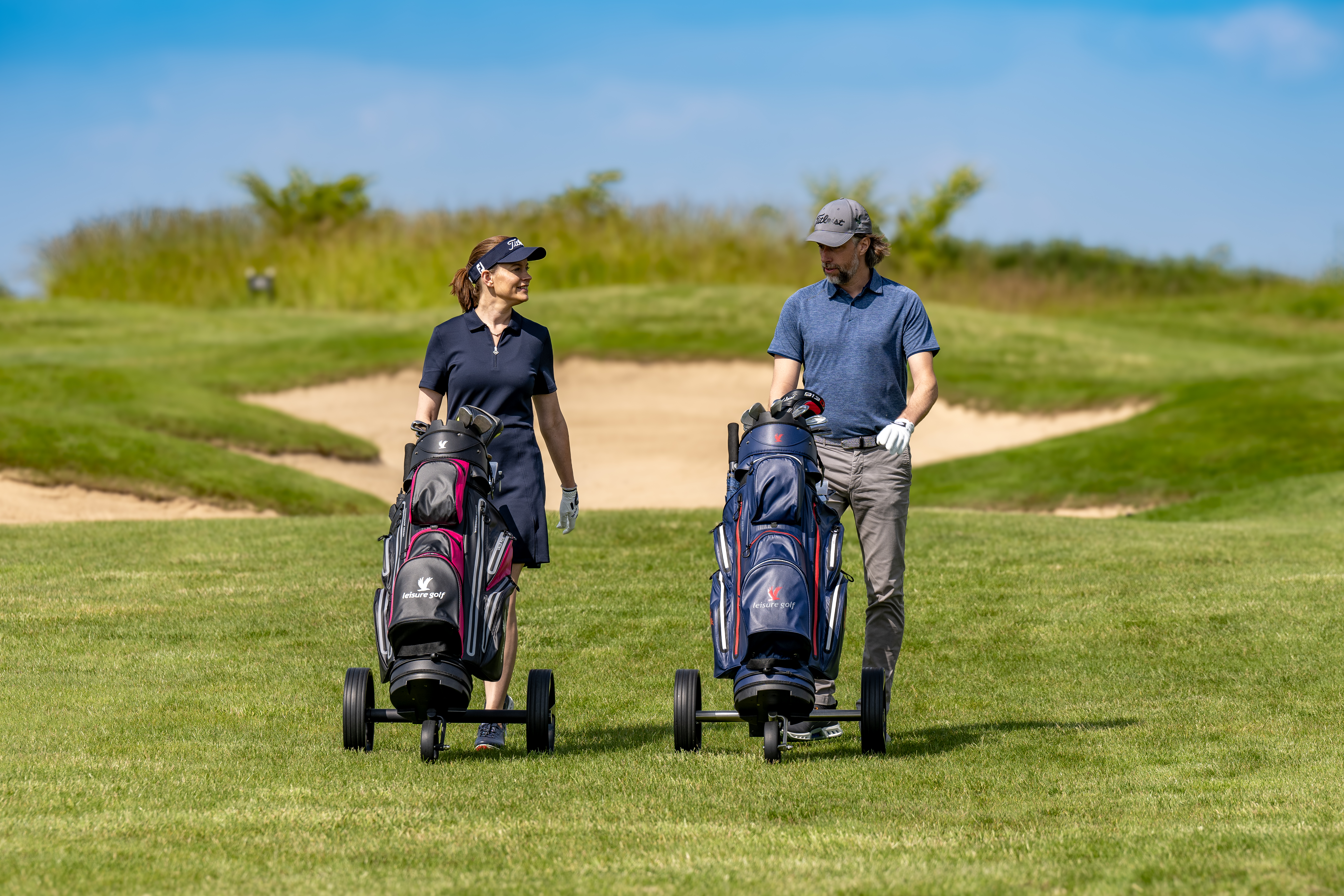 Ein Paar läuft mit ihren Golf Trolleys über den Golfplatz