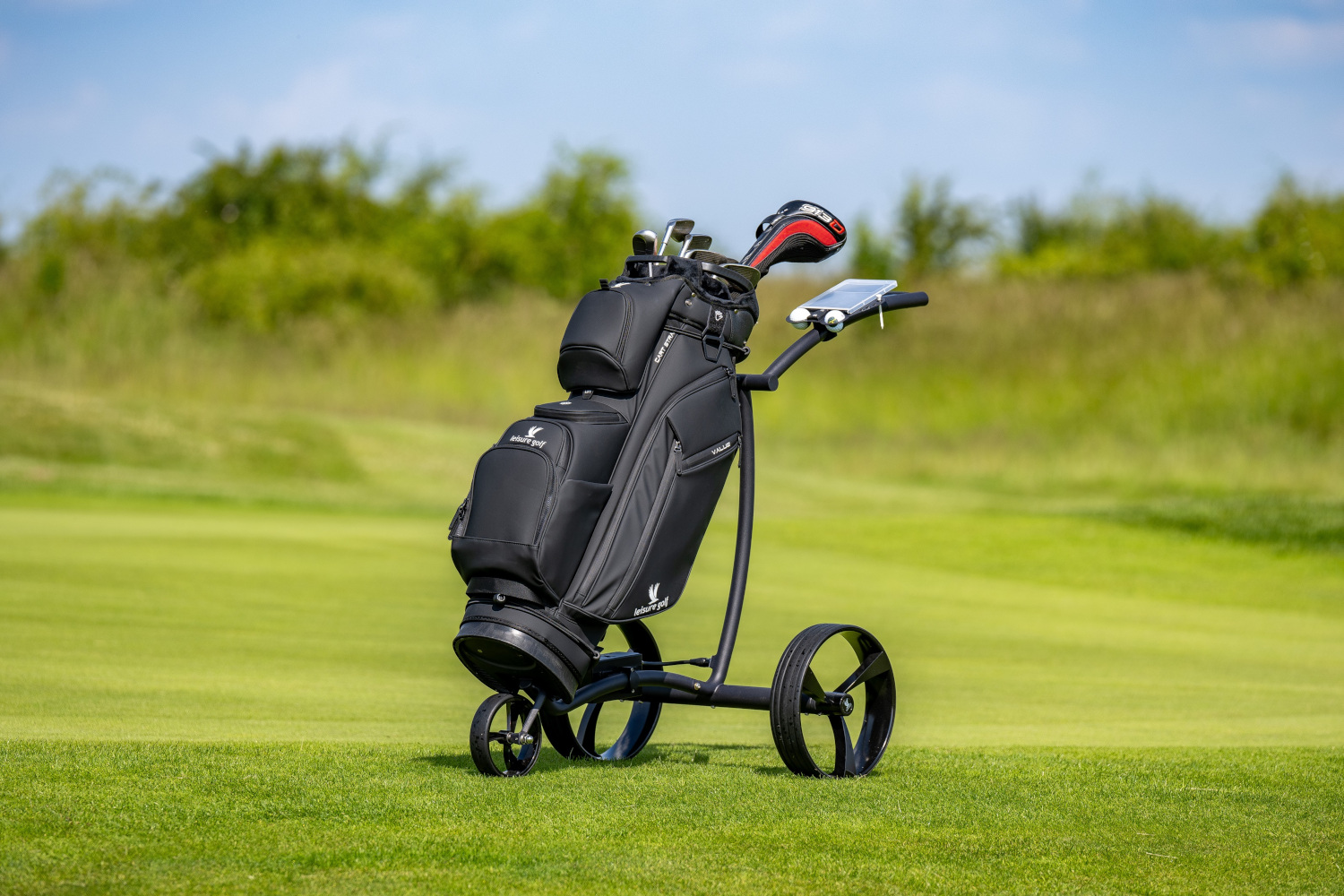 Schwarzer Golftrolley mit schwarzer Golfbag auf einer Wiese